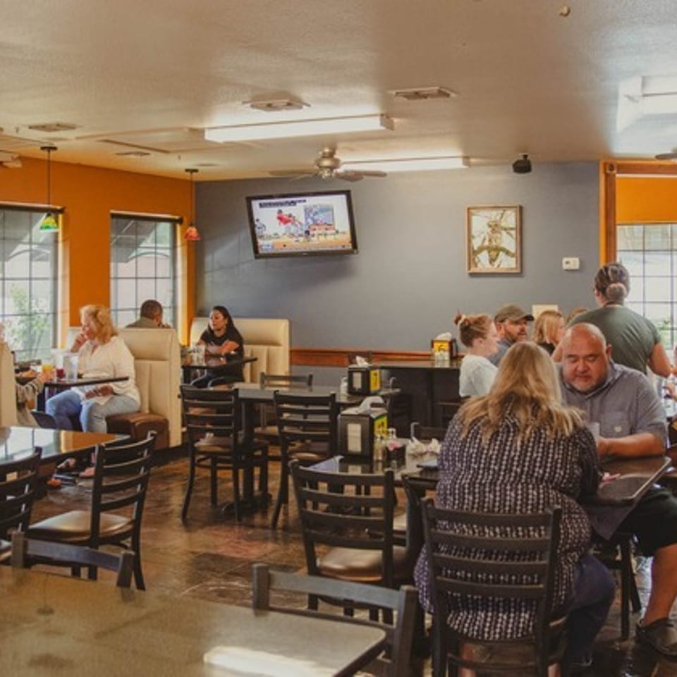 Busy casual restaurant dining room with orange walls, booths, tables, ceiling fans, and groups of customers eating.