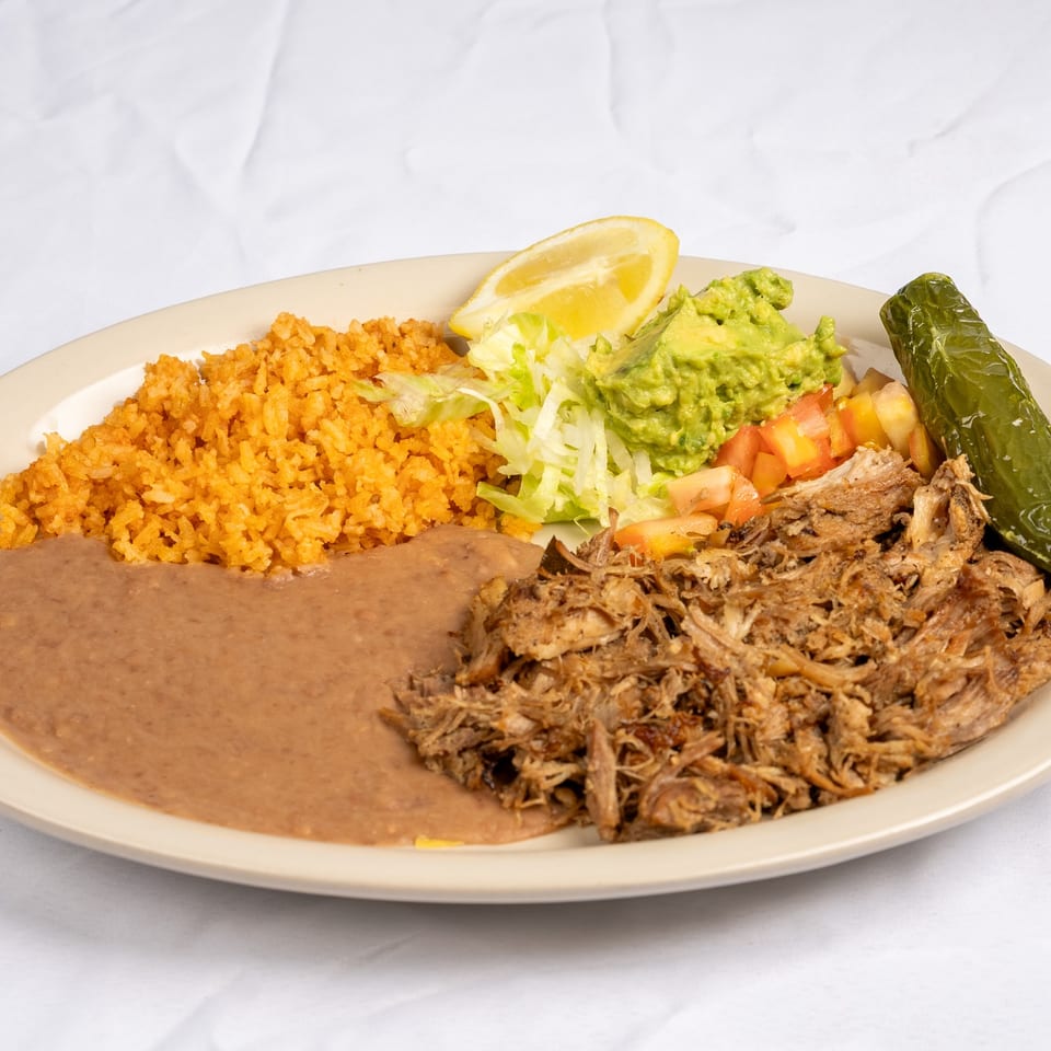 Carnitas plate with guacamole and a lemon wedge.